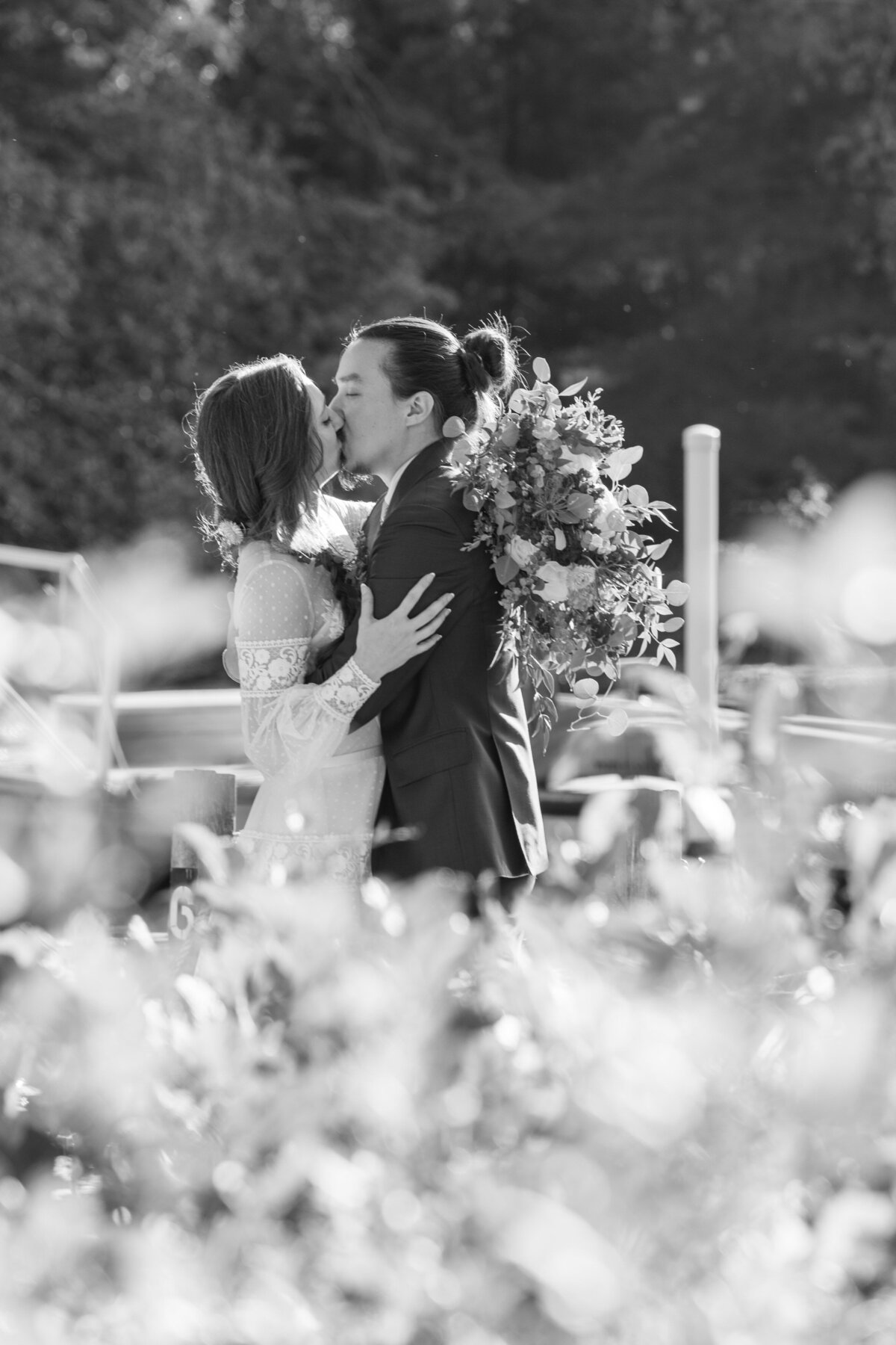 Black and white photo of a person kissing their partner in a field on their wedding day 