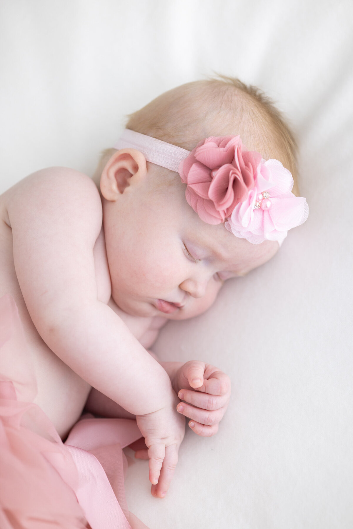 En baby iført rosa hårbånd og rosa tyllskjørt sover på et hvitt teppe. Fotografert i Studio Landmark, Fyllingsdalen.