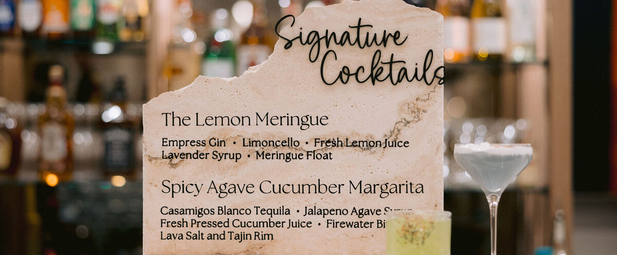 A travertine stone bar sign with specialty cocktails on it.