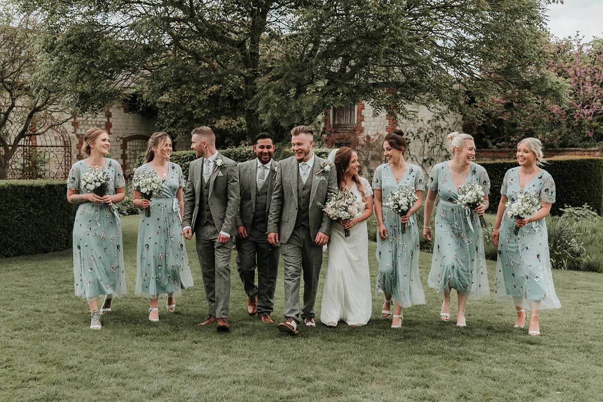 Wedding couple and their wedding party walking and laughing together at their wedding at Bury Court Farnham