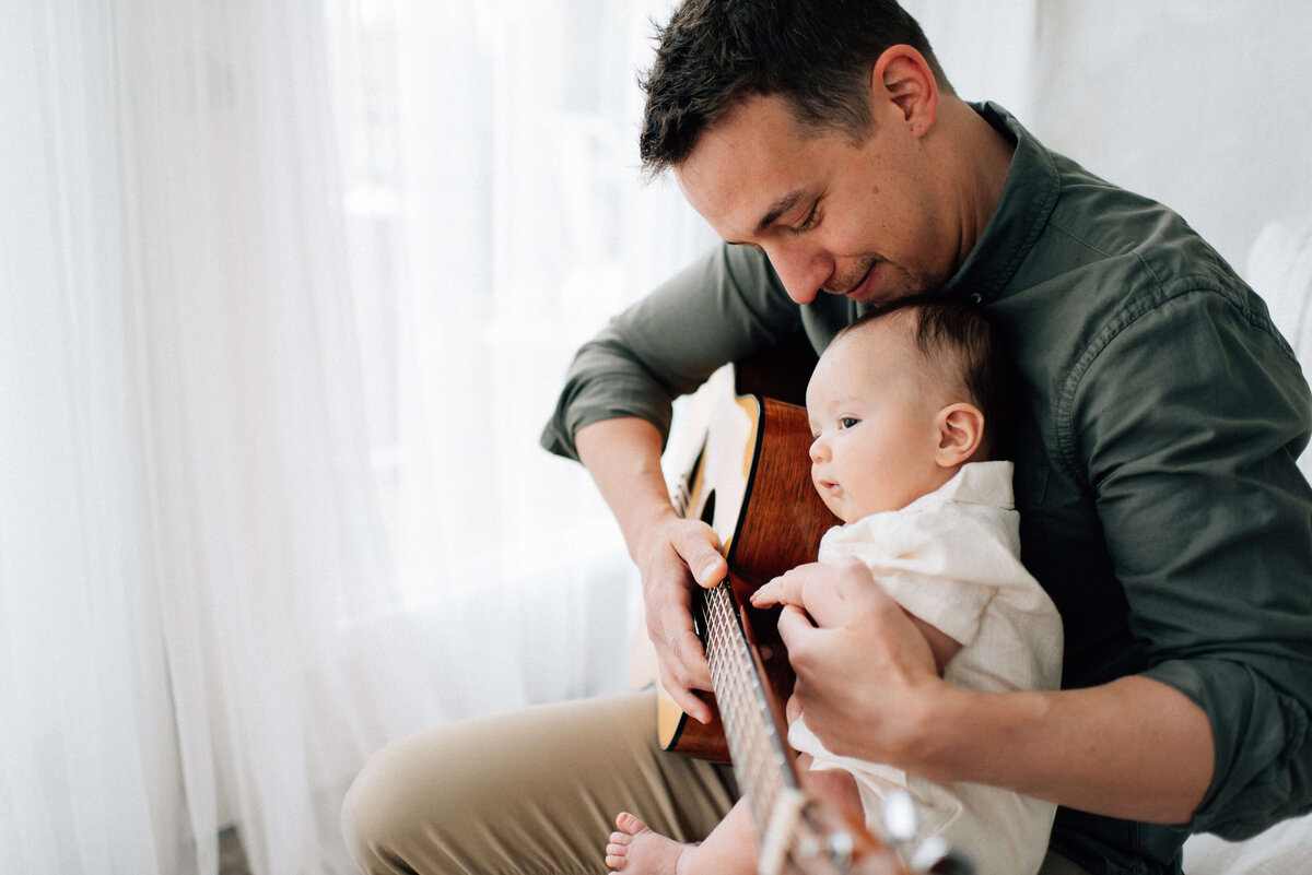 dad holding baby son on his lap while he plays the guitar