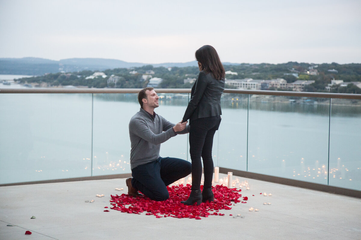 A man kneels down to propose to a woman on a balcony during an intimate moment captured by an Austin wedding photographer.