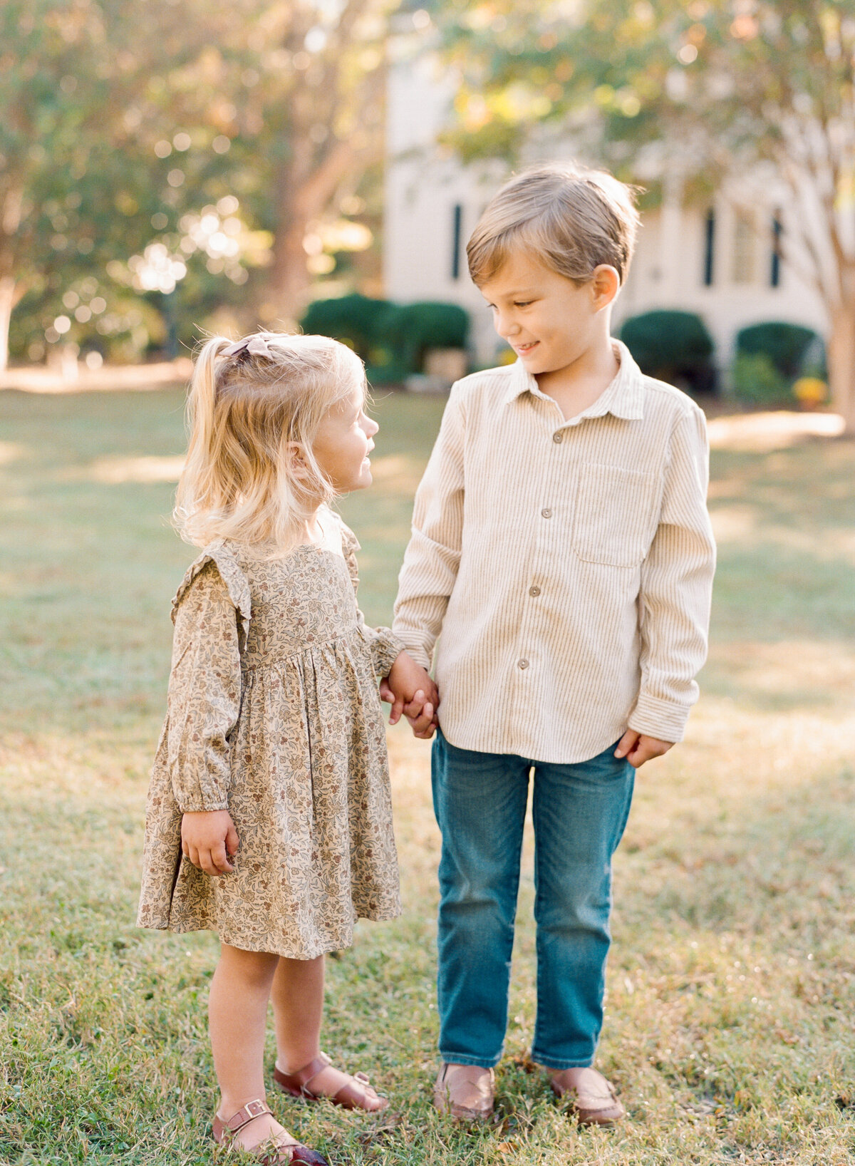 Siblings hold hands and smile at each other. Image by Raleigh maternity photographer A.J. Dunlap Photography.