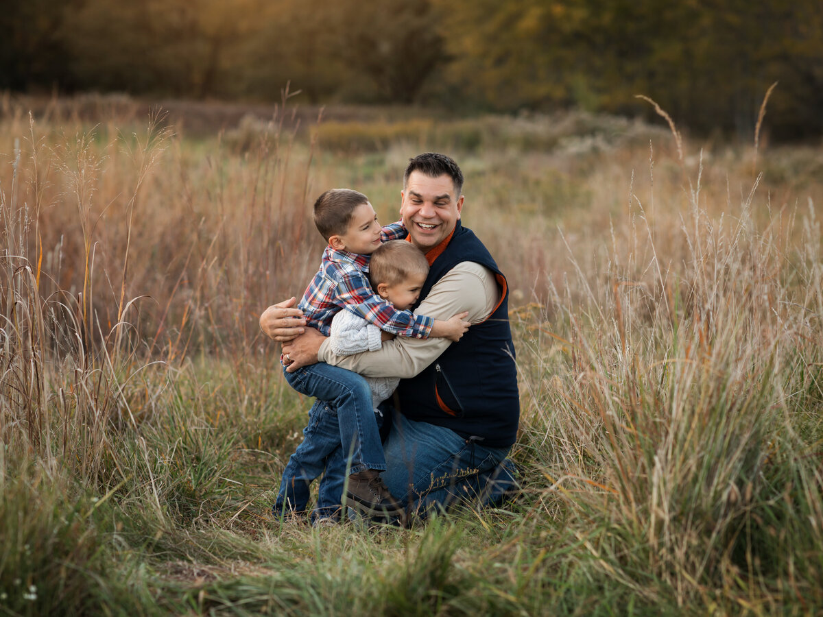 dad and two sons hugging in field for family photos