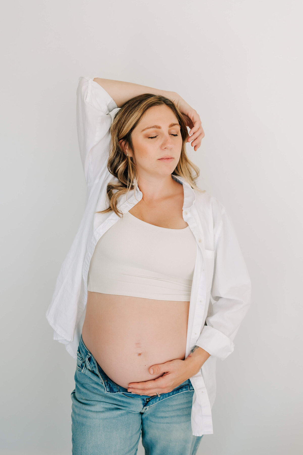 pregnant mom in jeans holding baby bump during studio maternity session in Springfield MO