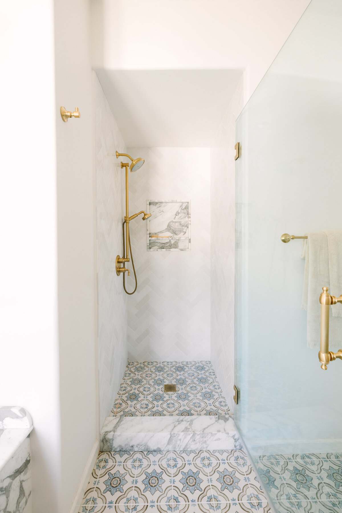 Primary bathroom with Chevron Chloe Tile, Arabescato Corchia marble niche, brass fixtures and patterned floor tile.