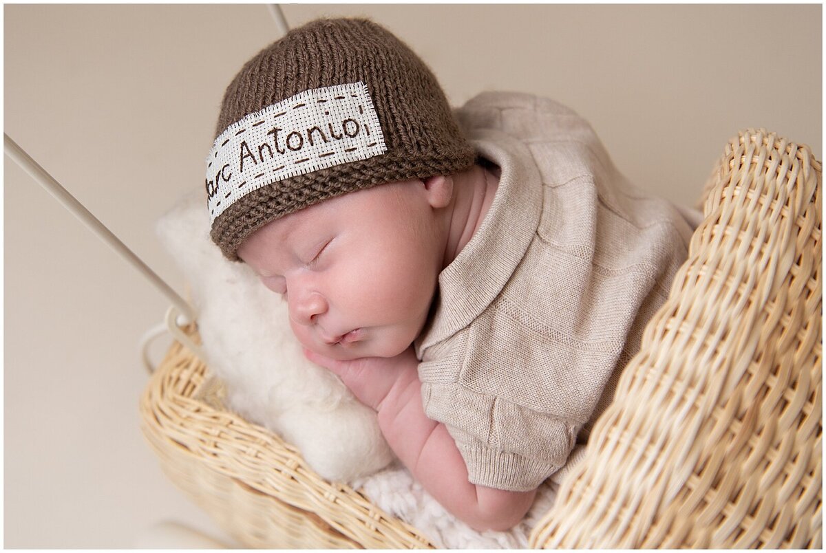 Close up image of a baby boy sleeping in a pram stroller, wearing a hat that has his name on it.