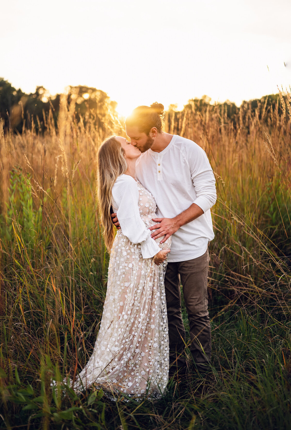 pregnant mom kissing husband in a field at sunset