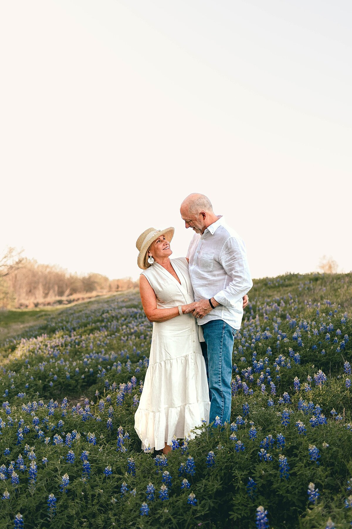 Older couple standing in bluebonnets holding hands and looking at each other smiling by Cypress Family Photographer
