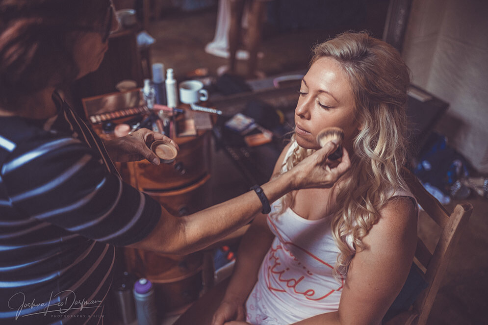 A woman sitting at a table having her makeup done