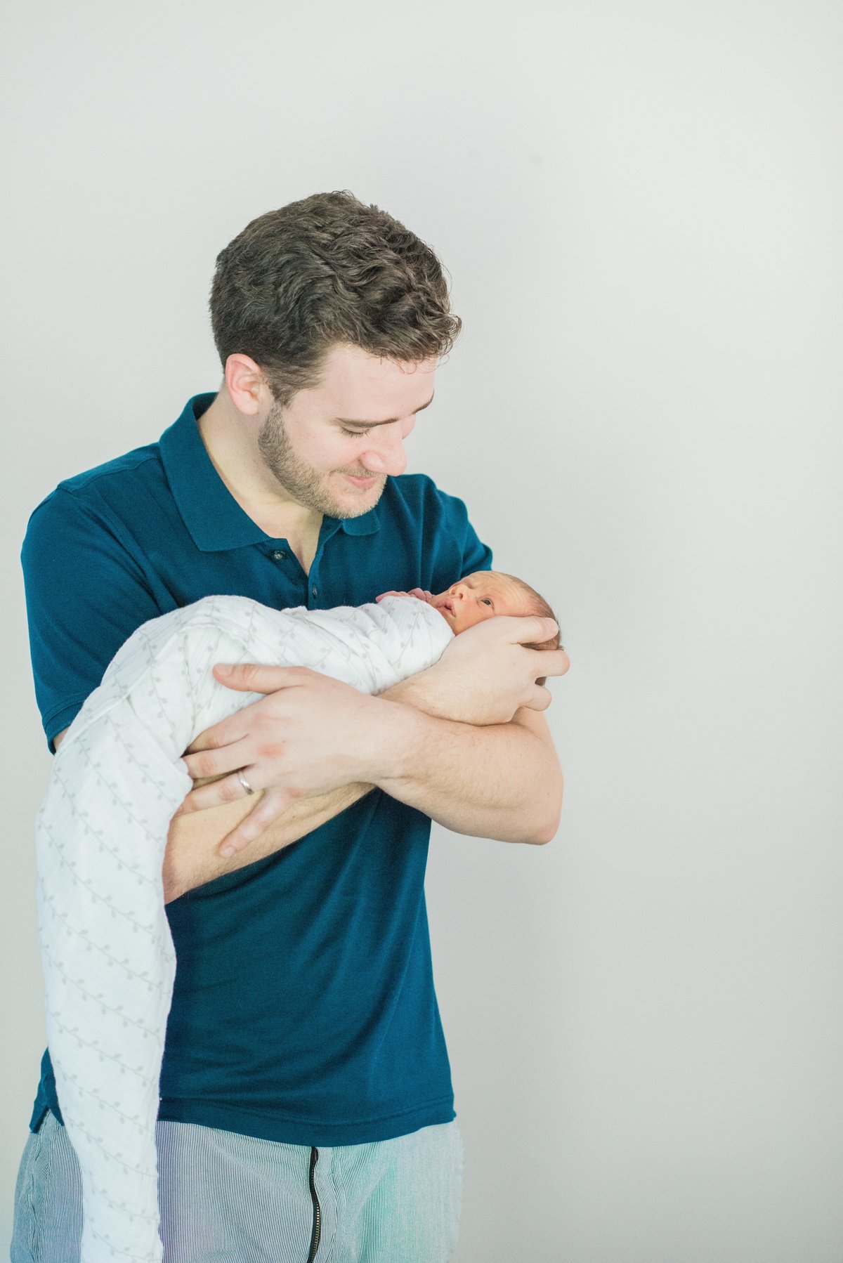 dad holding first son in navy collared shirt and baby in white swaddle