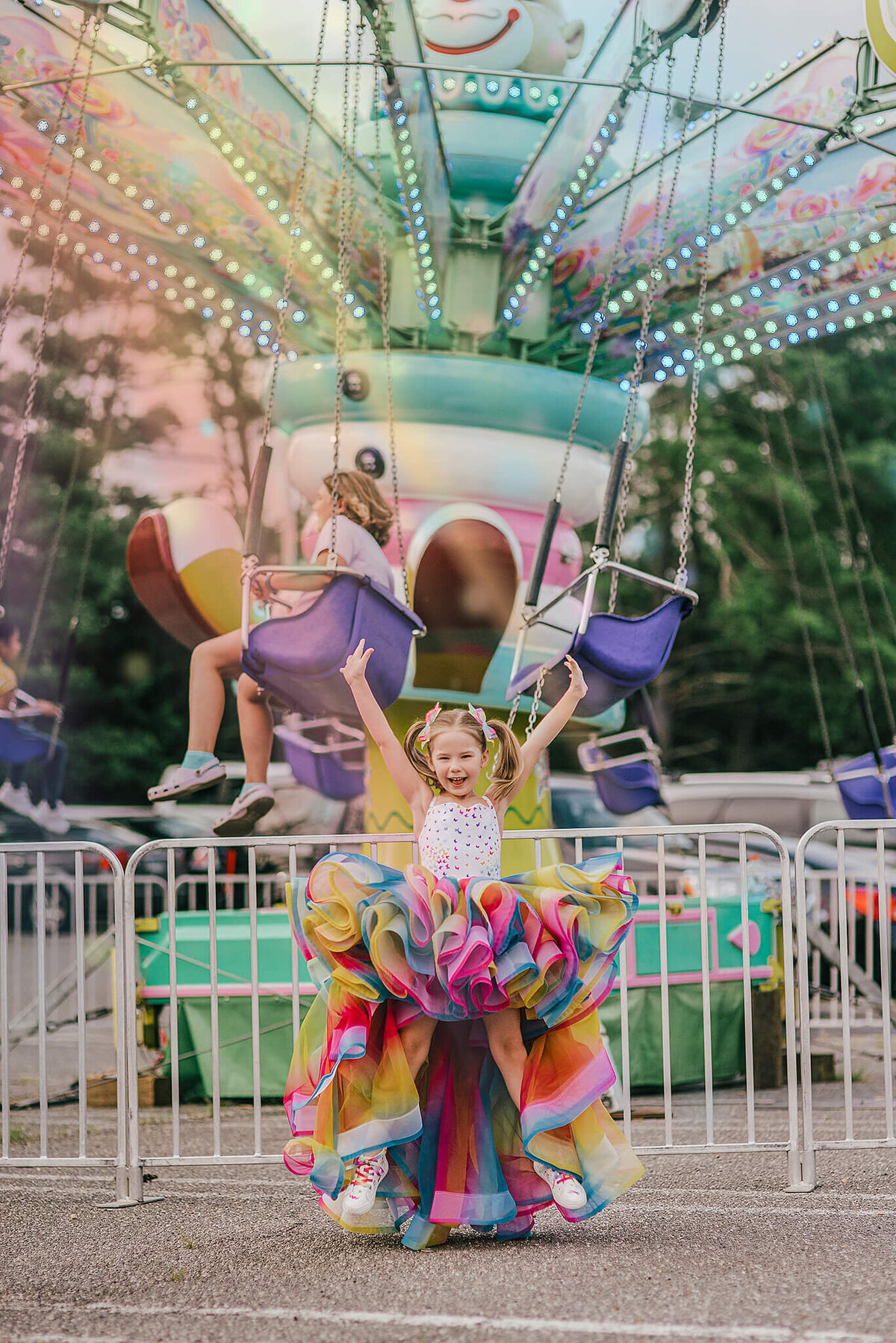 Girl in pigtails wearing a rainbow dress and jumping in front of a carnival ride near Annapolis Maryland