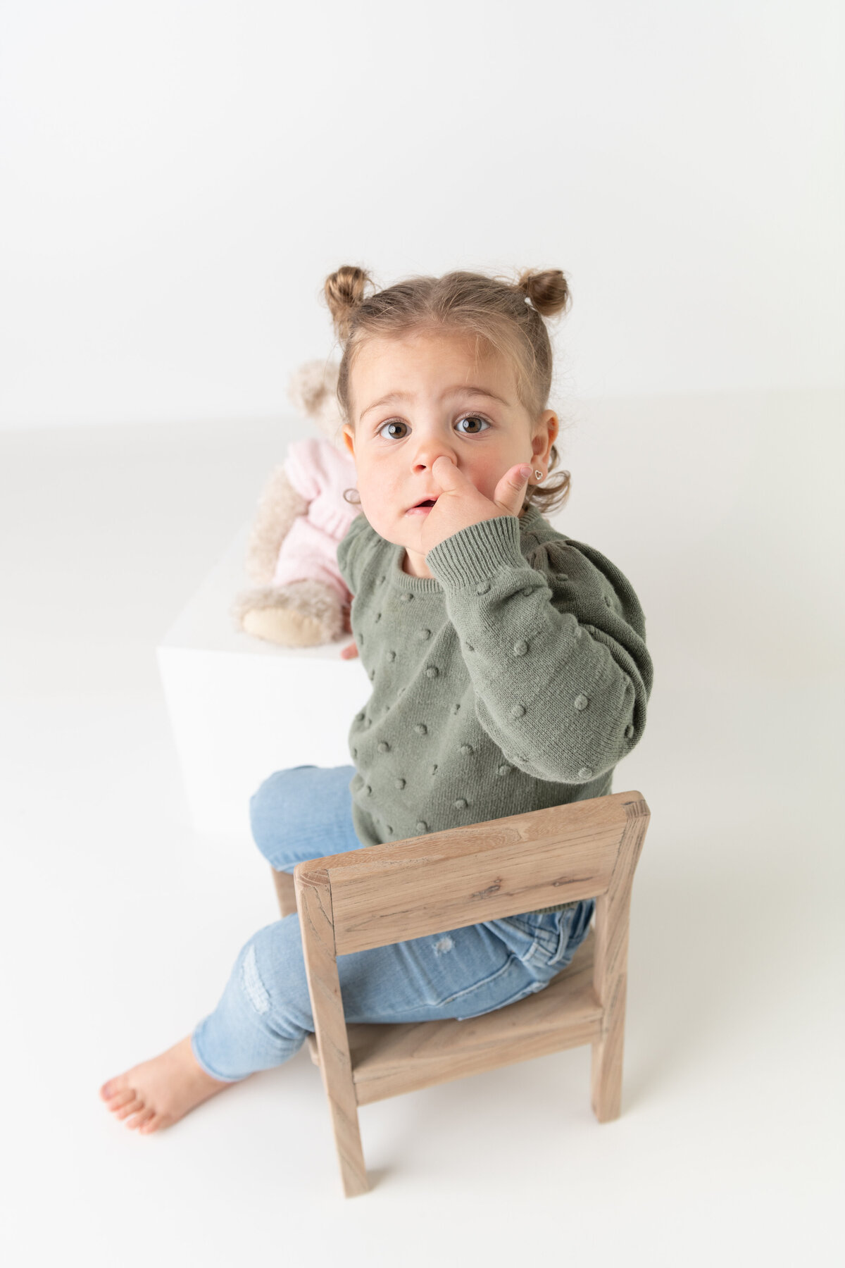 Milestone studio portrait of a toddler girl beside her teddy, captured in a quiet moment of wonder and comfort.