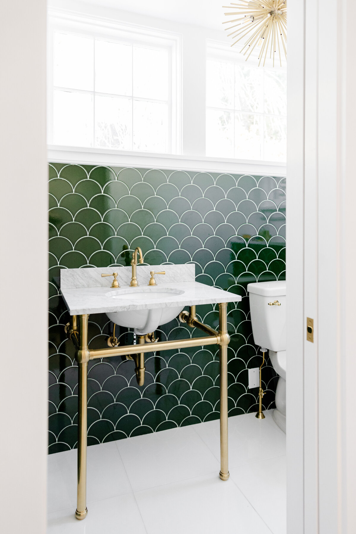 The bathroom boasts gold hardware, and emerald green ceramic tiles.