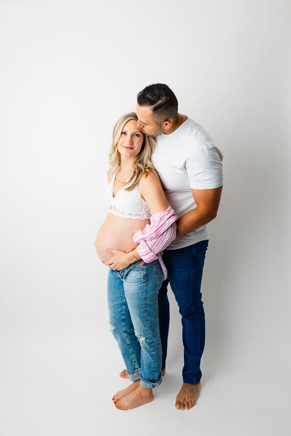 A man stands behind his pregnant wife and kisses her head.