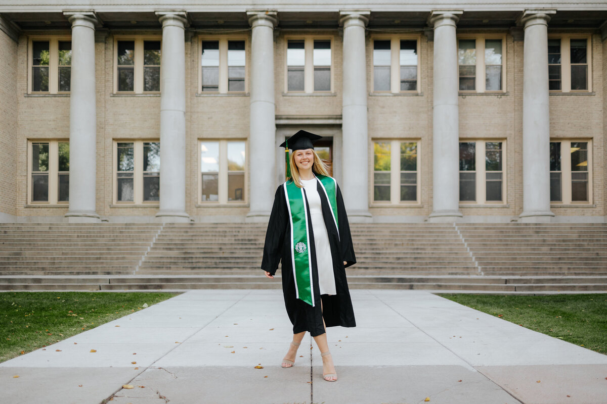 A Colorado State University graduate walks confidently toward the camera outside the Administration Building in Fort Collins, Colorado.