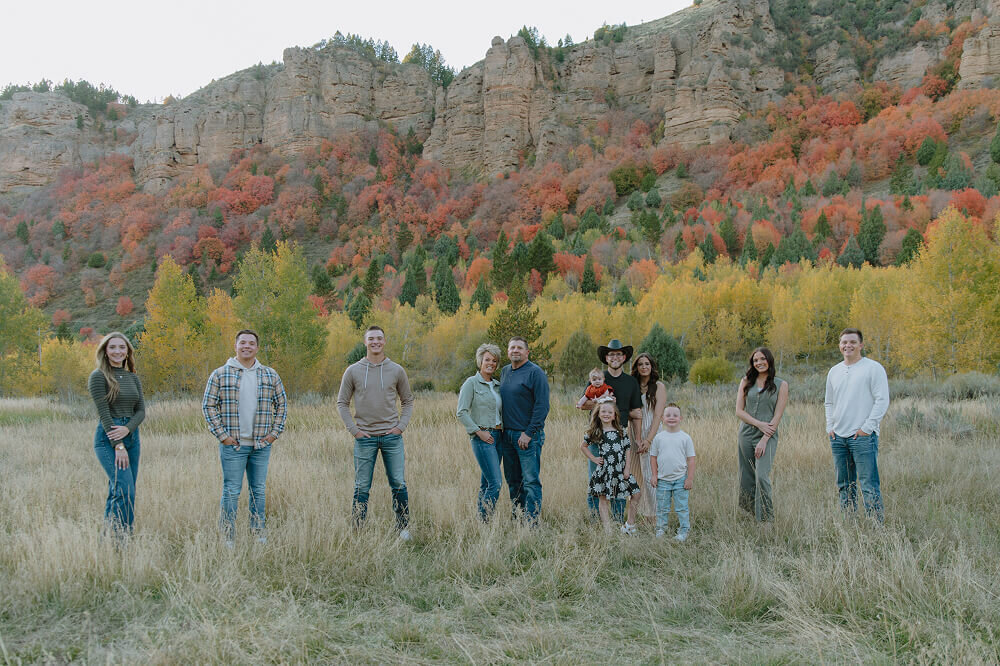 A family portrait where each family member has a little bit of space between them. There are 2 sons, a mother and father, one of their married children and her spouse and kids, a daughter, and one more son.