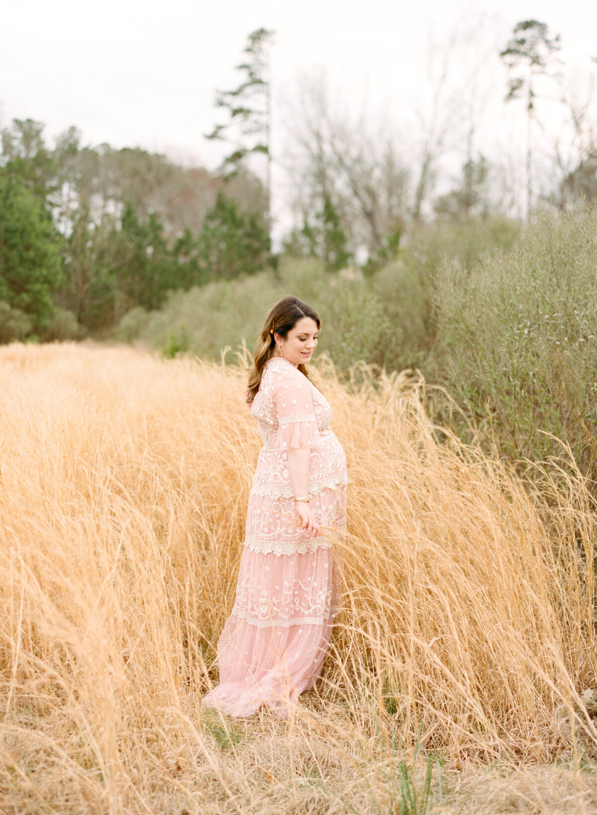 Mom stands in a field and cradles her growing belly during her Durham NC maternity session. Image by Raleigh maternity photographer A.J. Dunlap Photography.