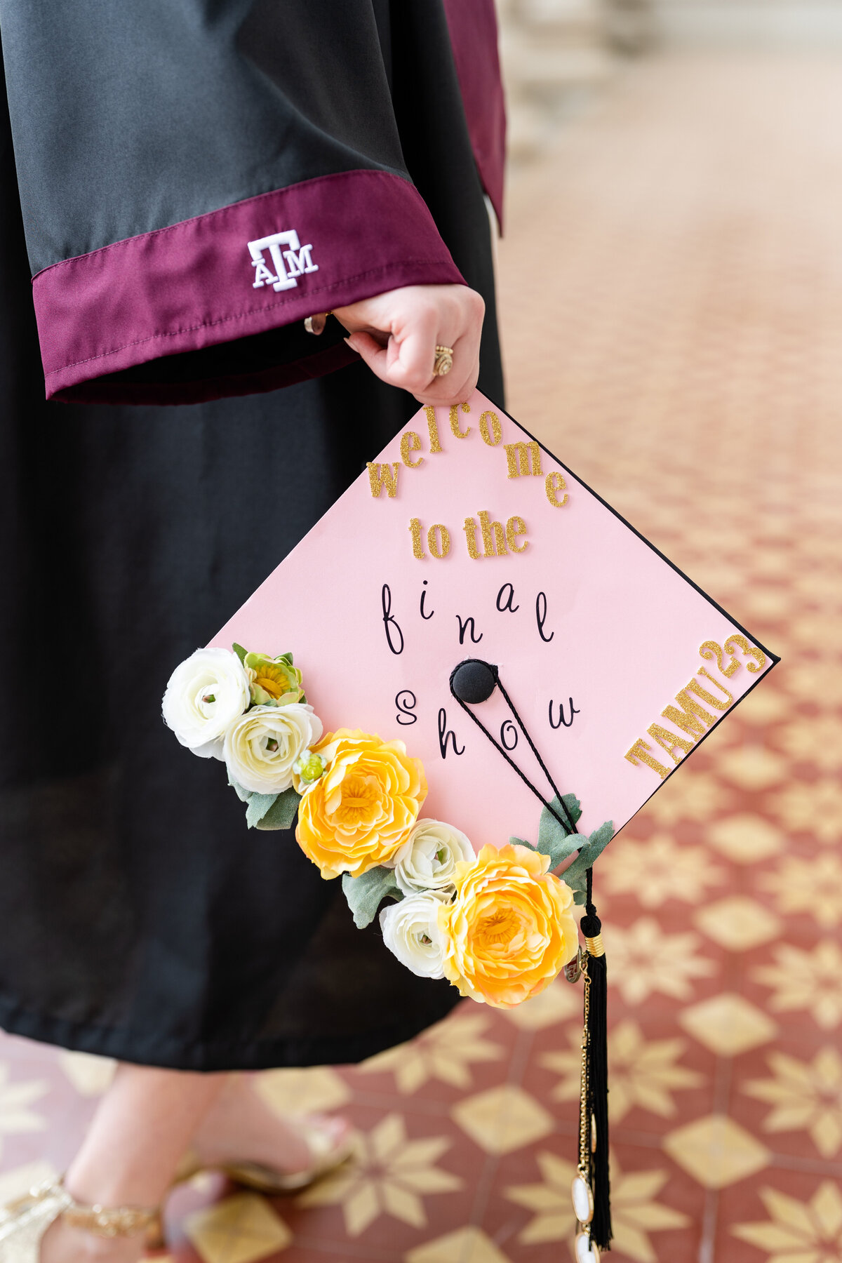 Texas A&M senior girl holding decorated grad cap that's pink with flowers down by her side