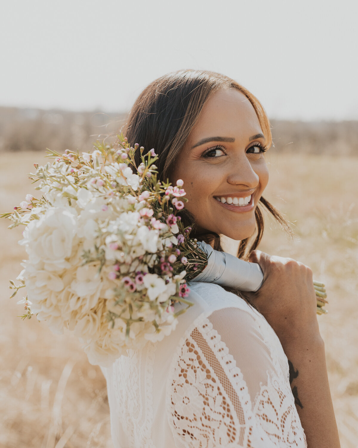 bride in field holding bouquet over shoulder