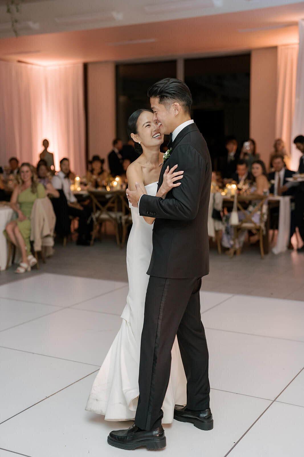 Bride and groom embrace during their intimate first dance at their Aspen Meadows Resort wedding reception, surrounded by friends and family.