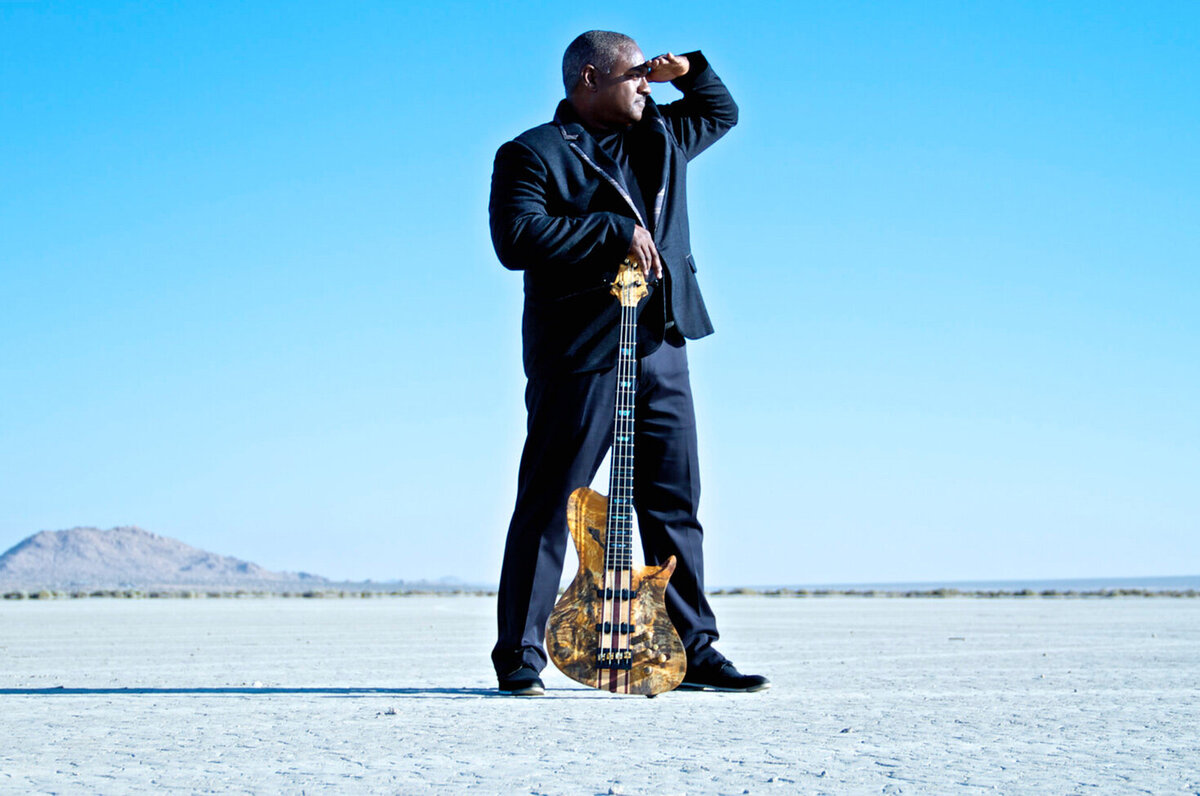 Musician portrait Mitchell Coleman Jr standing in desert hand resting on  electric guitar standing upright between his legs other hand shielding his eyes Just Play Something Gallery
