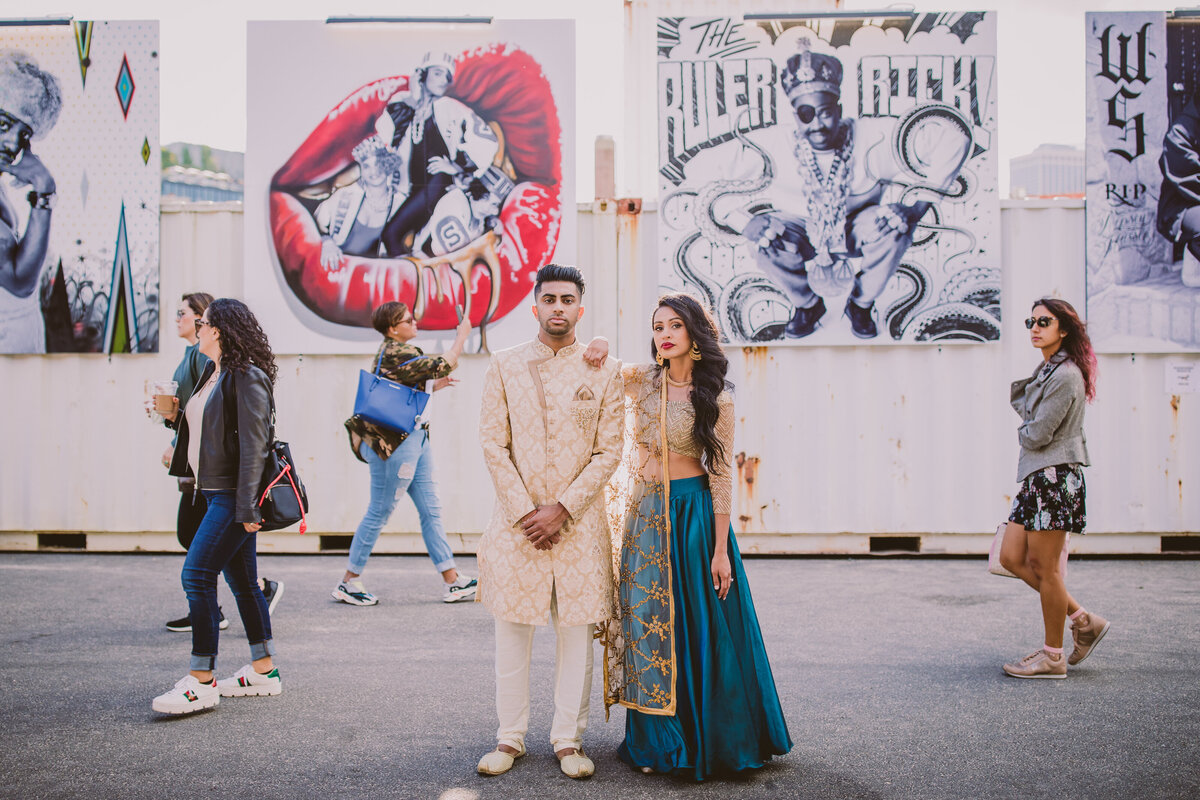 A couple posing for the camera during their engagement session in indian outfits at brooklyn bridge park in dumbo in front of an art exhibition