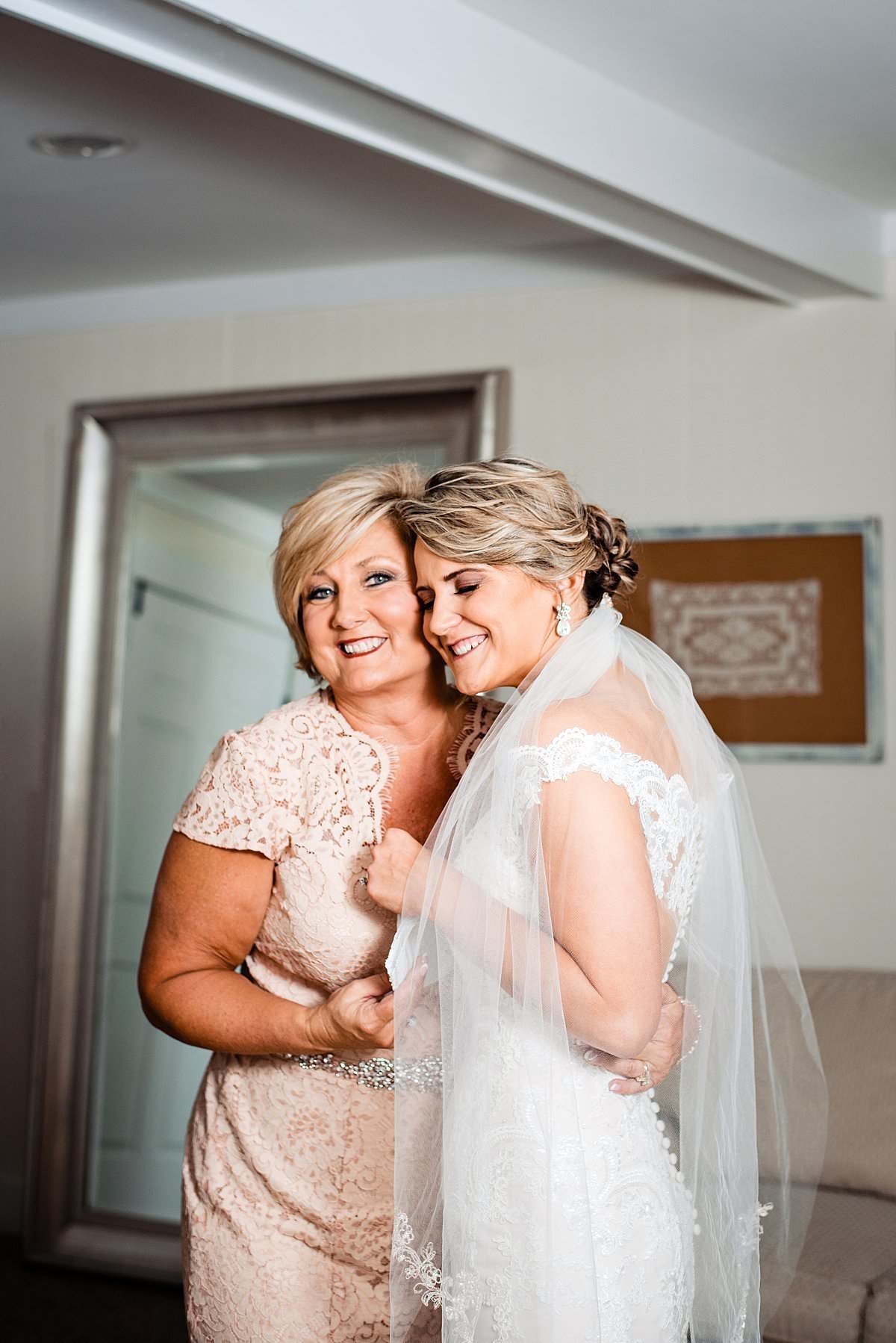 Mother of bride smiling at camera while her daughter hugs her