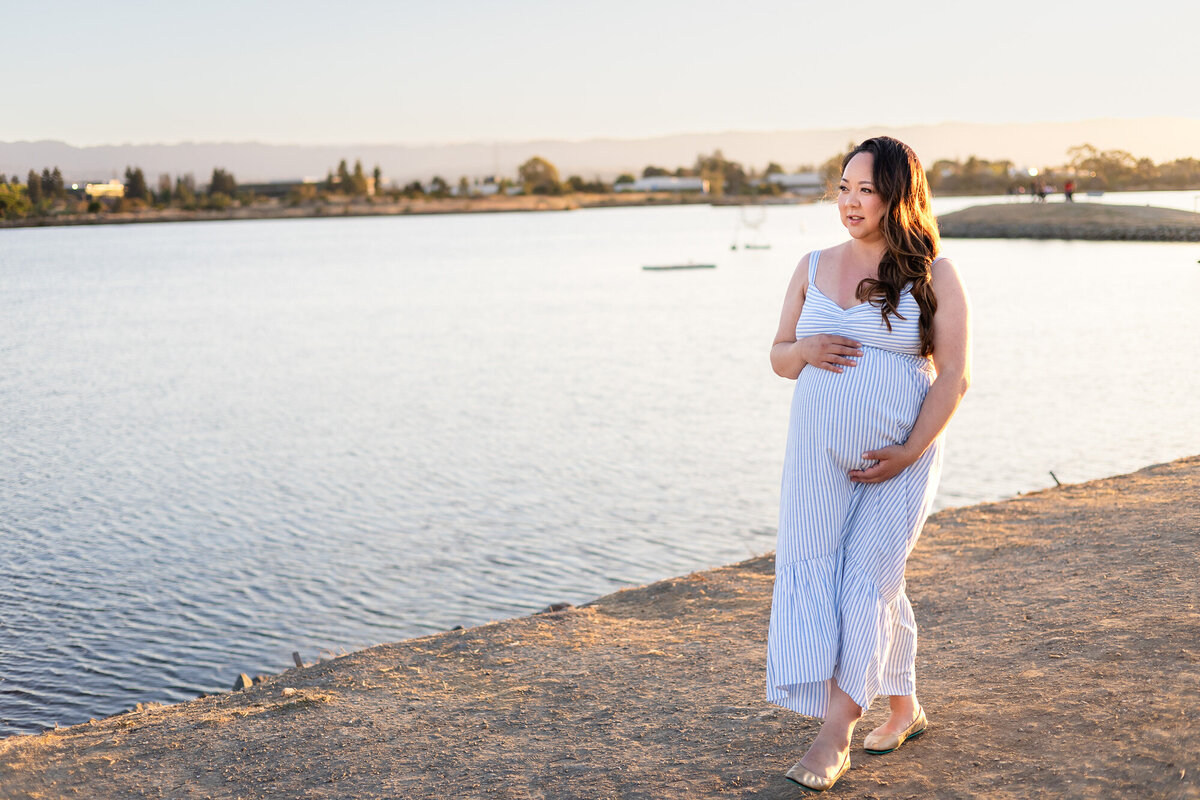 Pregnant woman standing by the water’s edge holding her belly at sunset — Bay Area Maternity Portfolio - Ellobelle Photography Family Photographer

