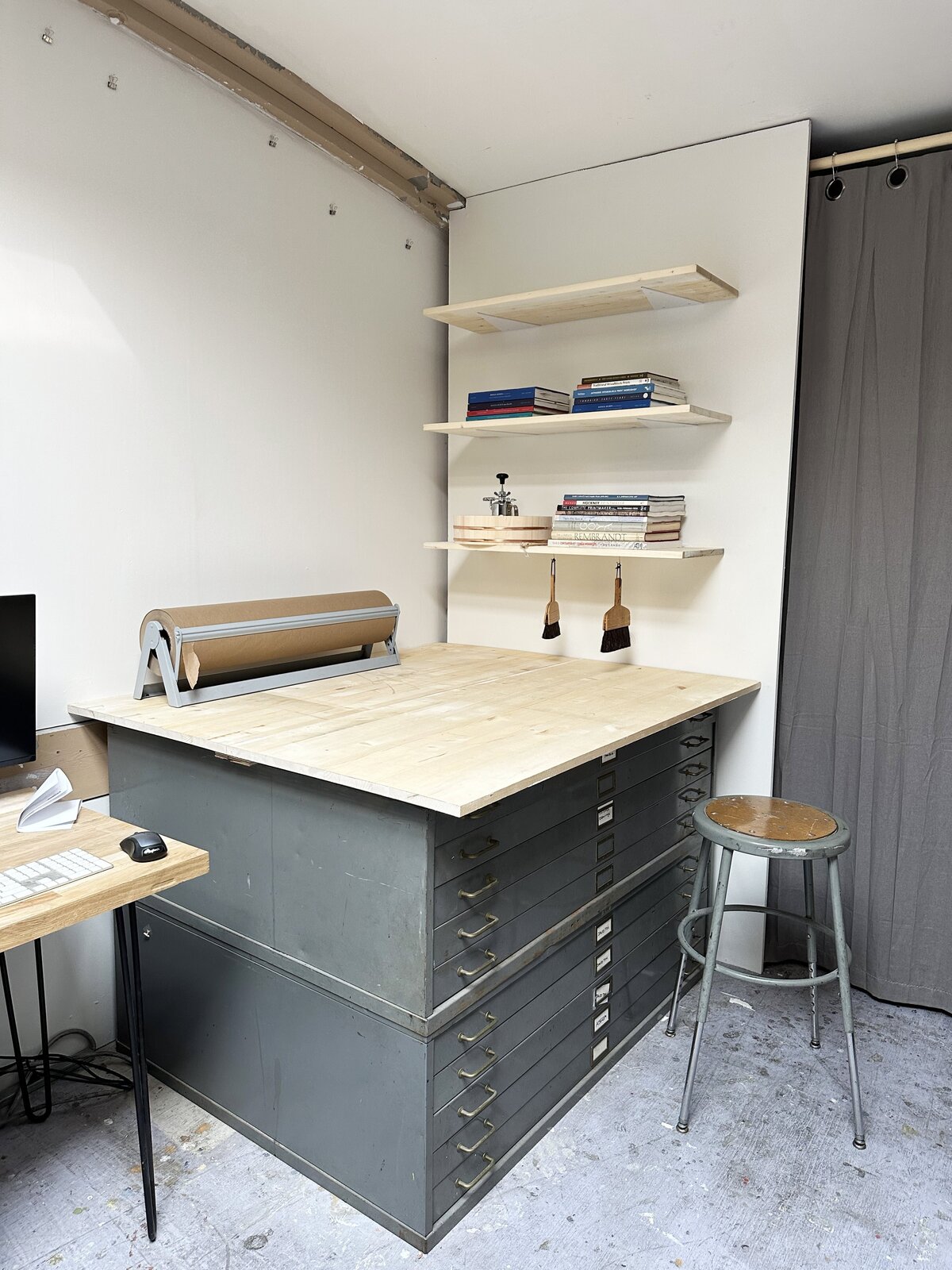 A printmaking studio workspace equipped with flat file drawers, a tabletop for projects, and shelves holding reference books and materials.