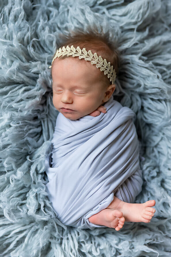Newborn baby girl wrapped in blue sleeps for her photo session.