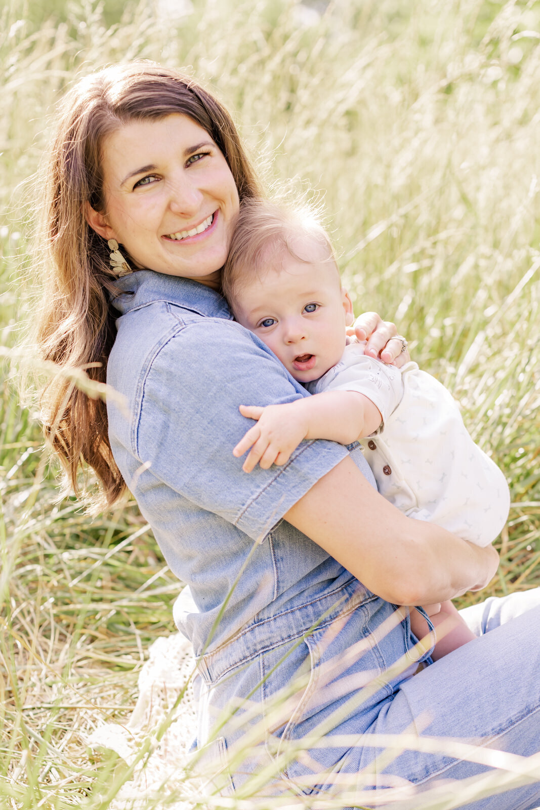 Mom hugs infant son in a field of tall grasses during a family photo session in Dacula