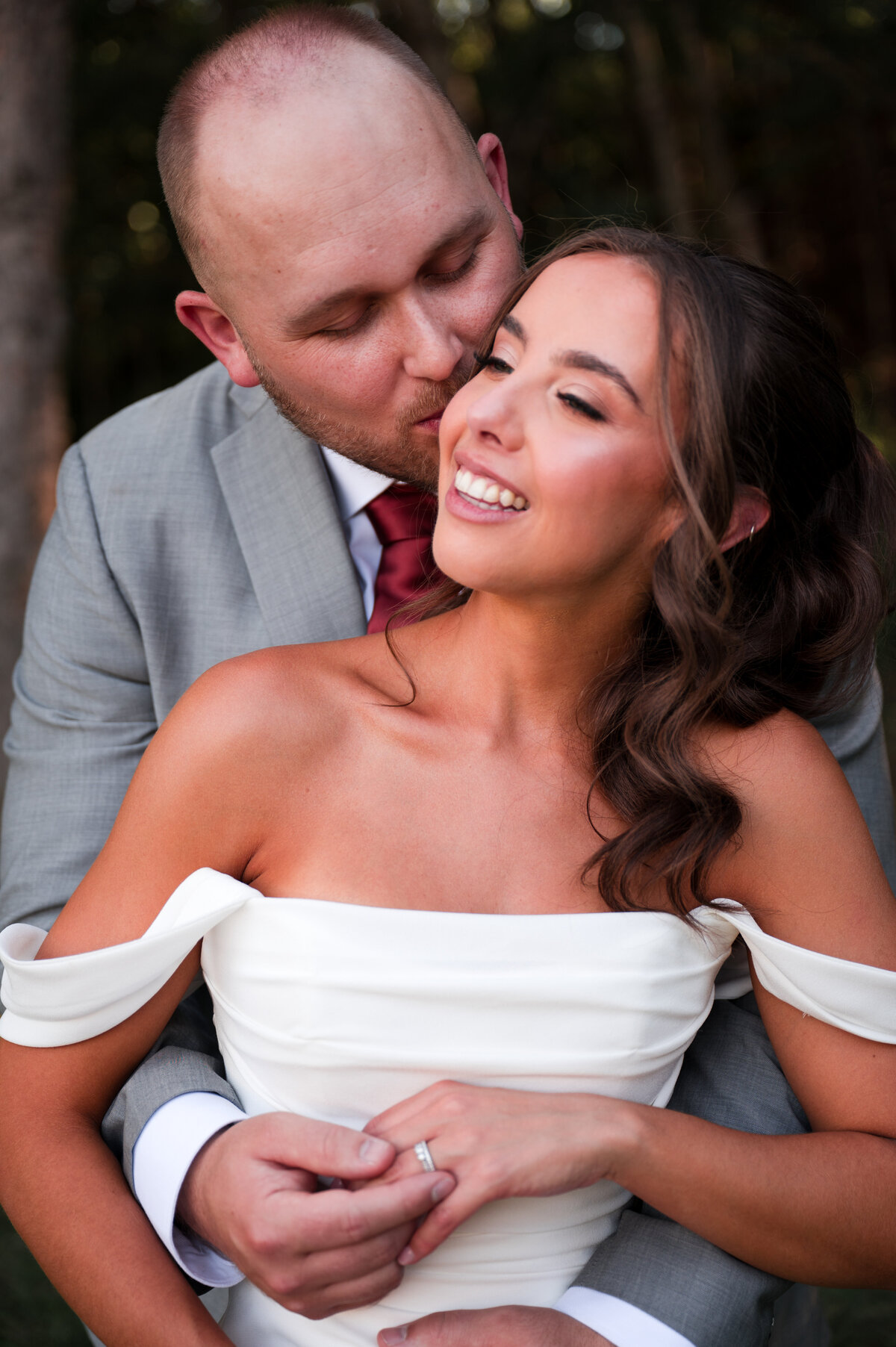 groom gives his bride a kiss on the cheet from behind