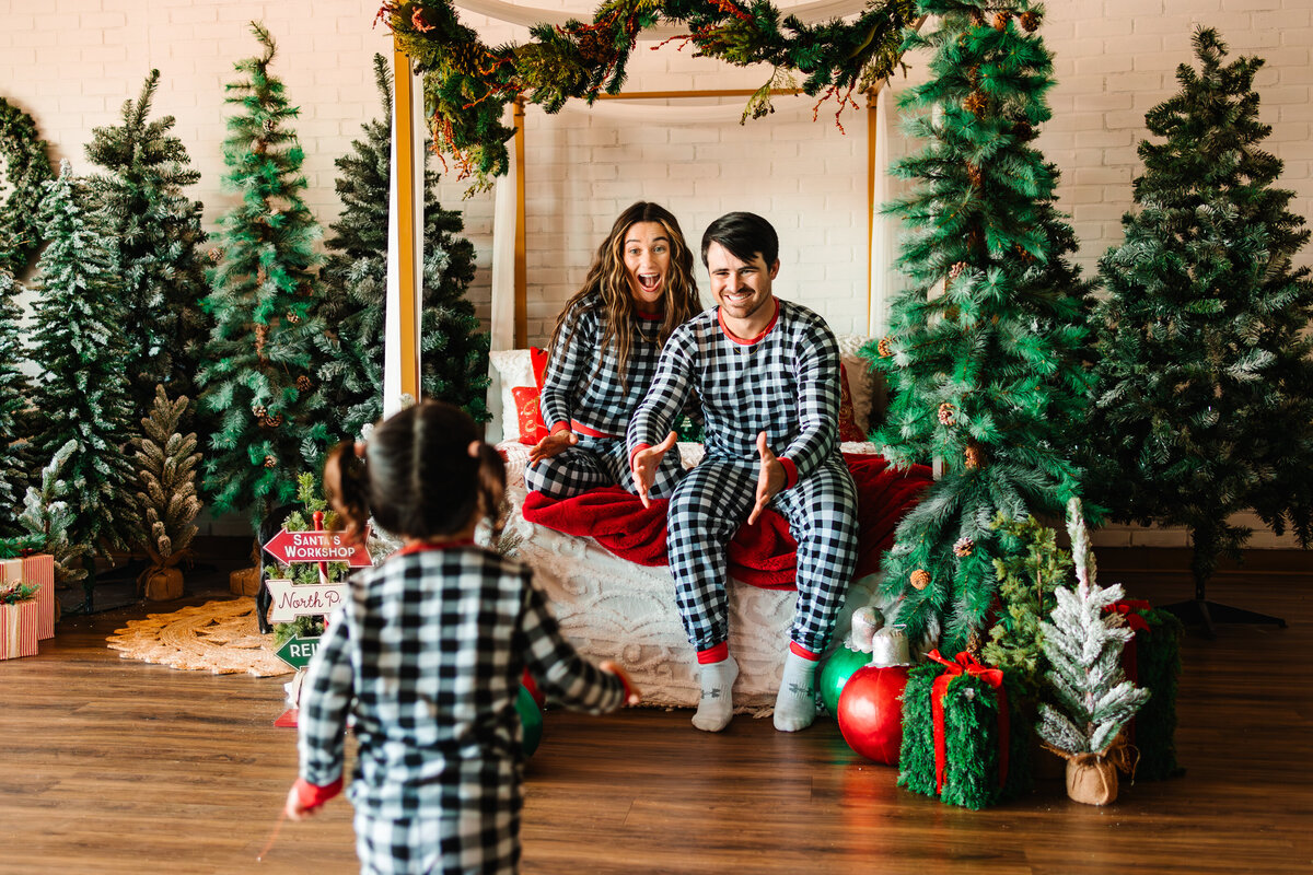 A mom and dad wait for their daughter to jump into their arms as she runs towards them at a holiday studio mini session in Albuquerque