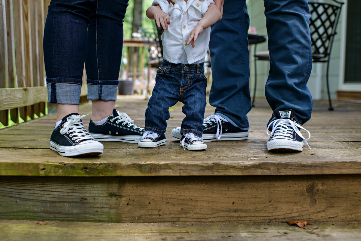 A family portrait of new parents and their baby in converse sneakers.