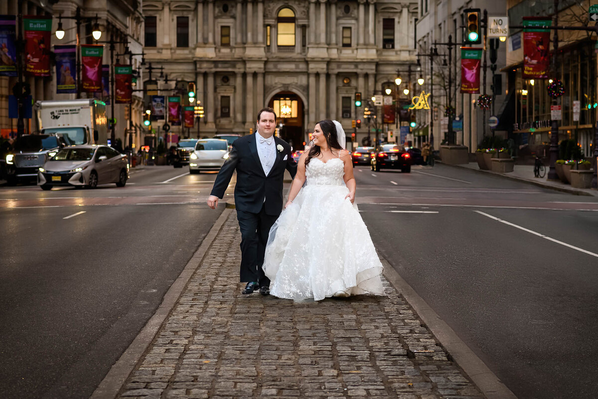 A wedding couple walks down the median of the street before City Hall