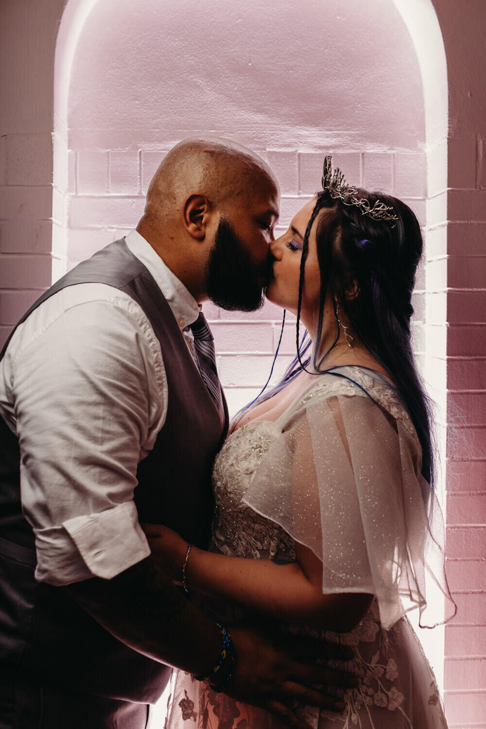 Bride and Groom kiss against pink backlit moody backdrop