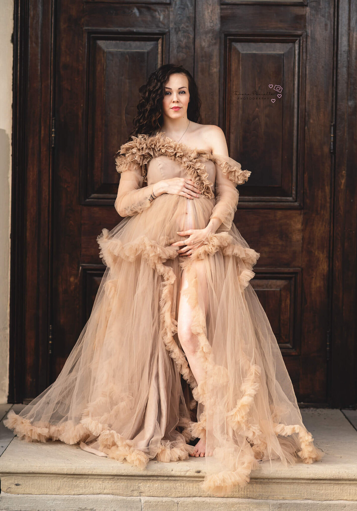 Expectant mom in a cream gown posed in front of a large door at Dundurn Castle.