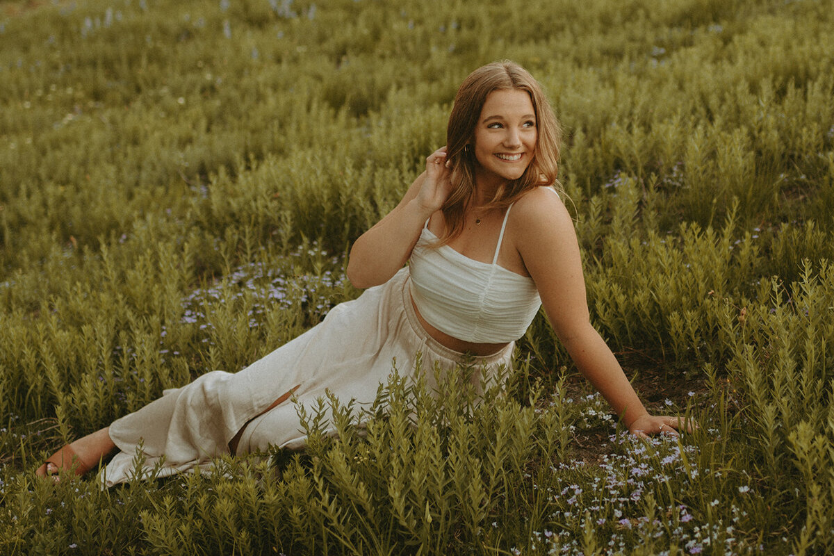 girl in white jumpsuit sitting in grassy field