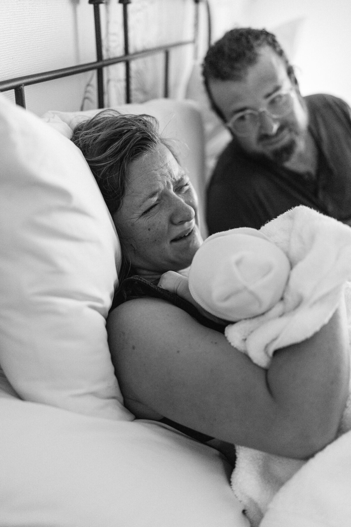 Sleeping newborn baby boy, swaddled in white blanket, peaceful expression, mom expressing relief 
