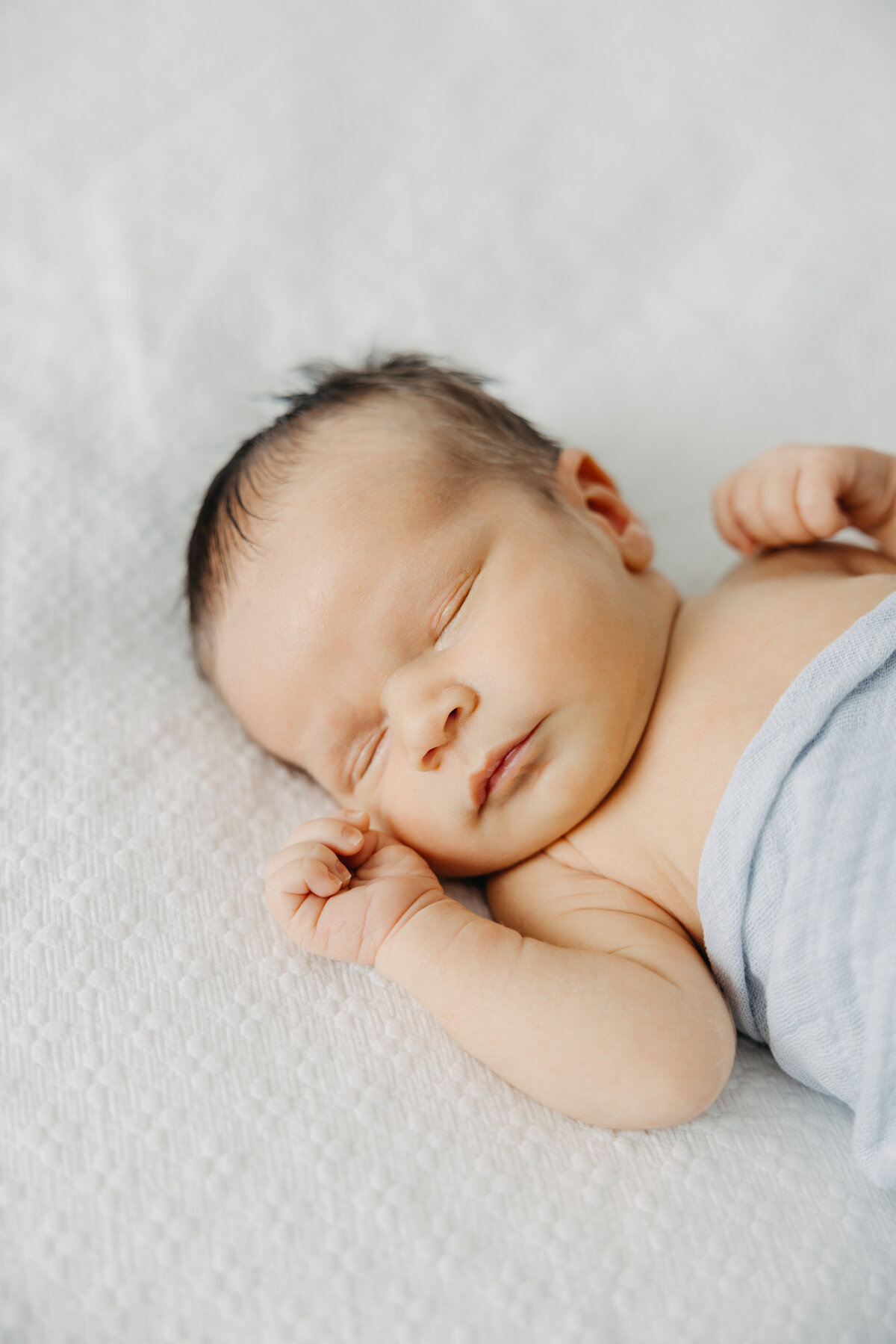 Newborn baby sleeping on bed with hands by face.