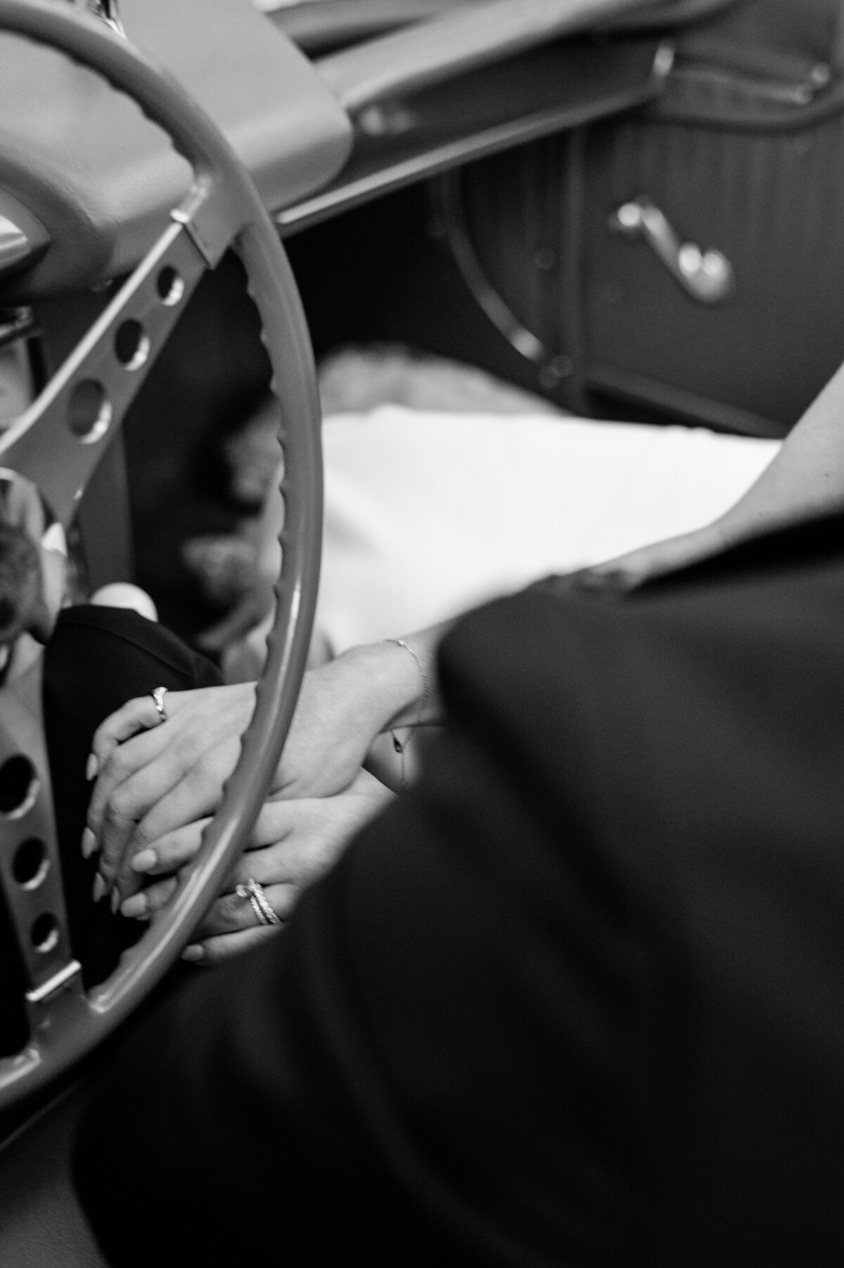 Bride and groom sit in their convertible holding hands 
