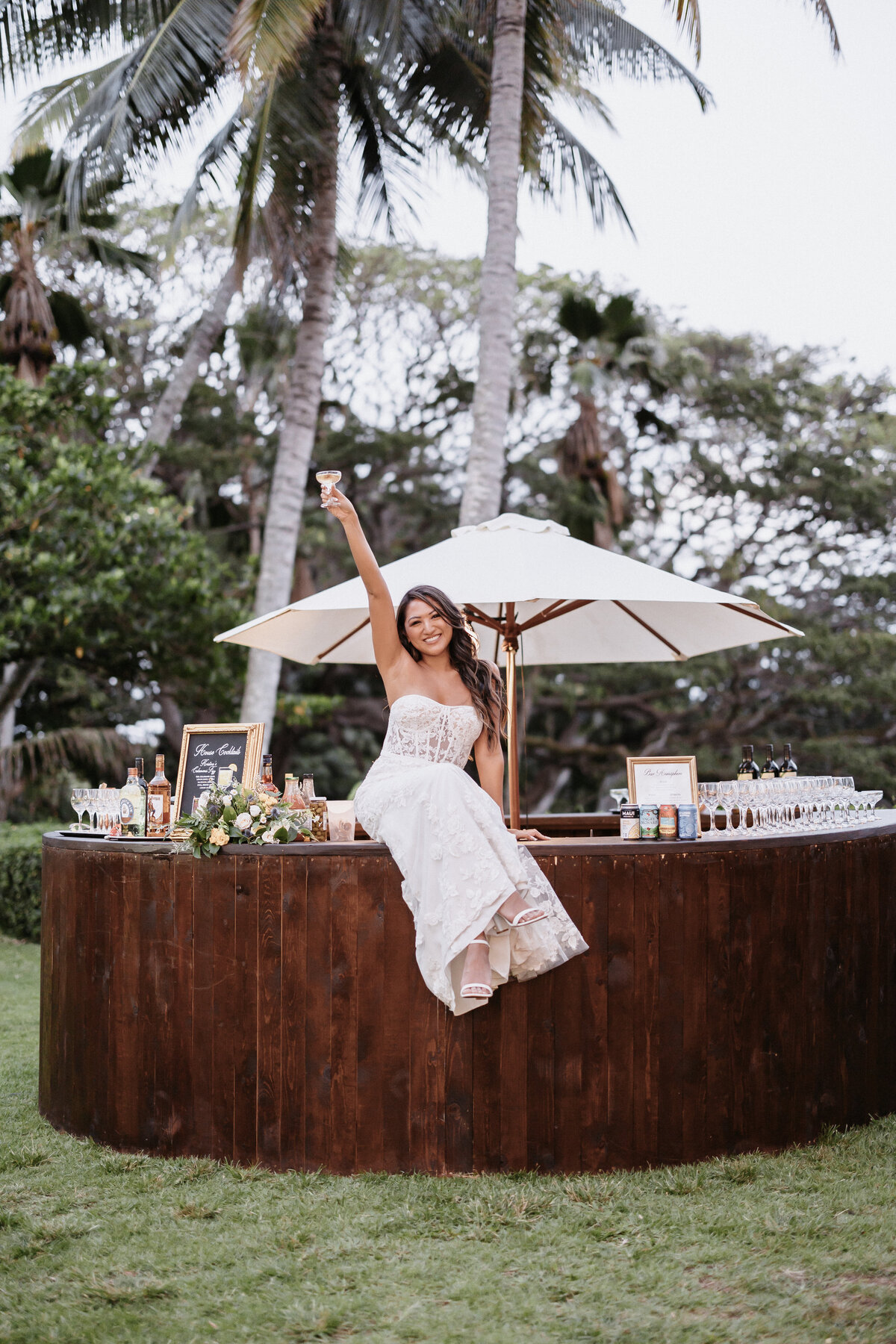 Bride sitting on dark wood bar raising a glass