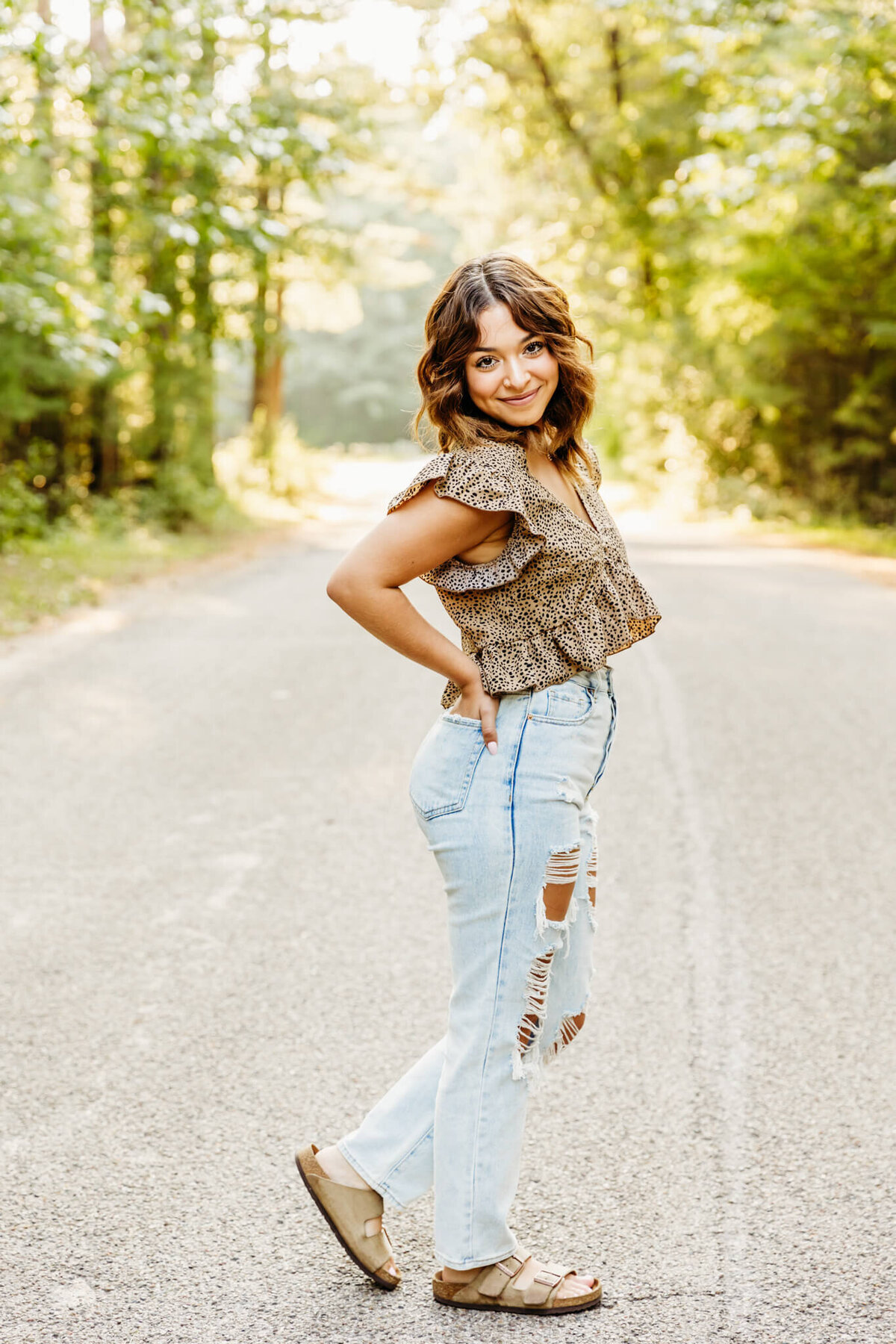 senior girl standing in the middle of the road with her foot kicked back and looking over her shoulder by Ashley Kalbus Photography