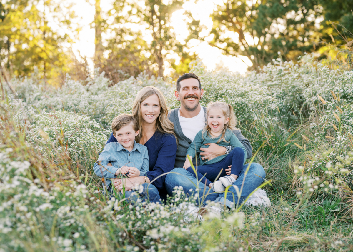 Family with young boy and girl smiling at camera on sunny day surrounded by white flowers