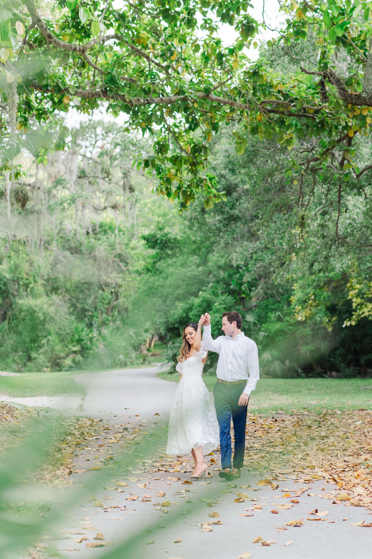 a couple holding hands walking while looking at each other and smiling and dancing on the woods
