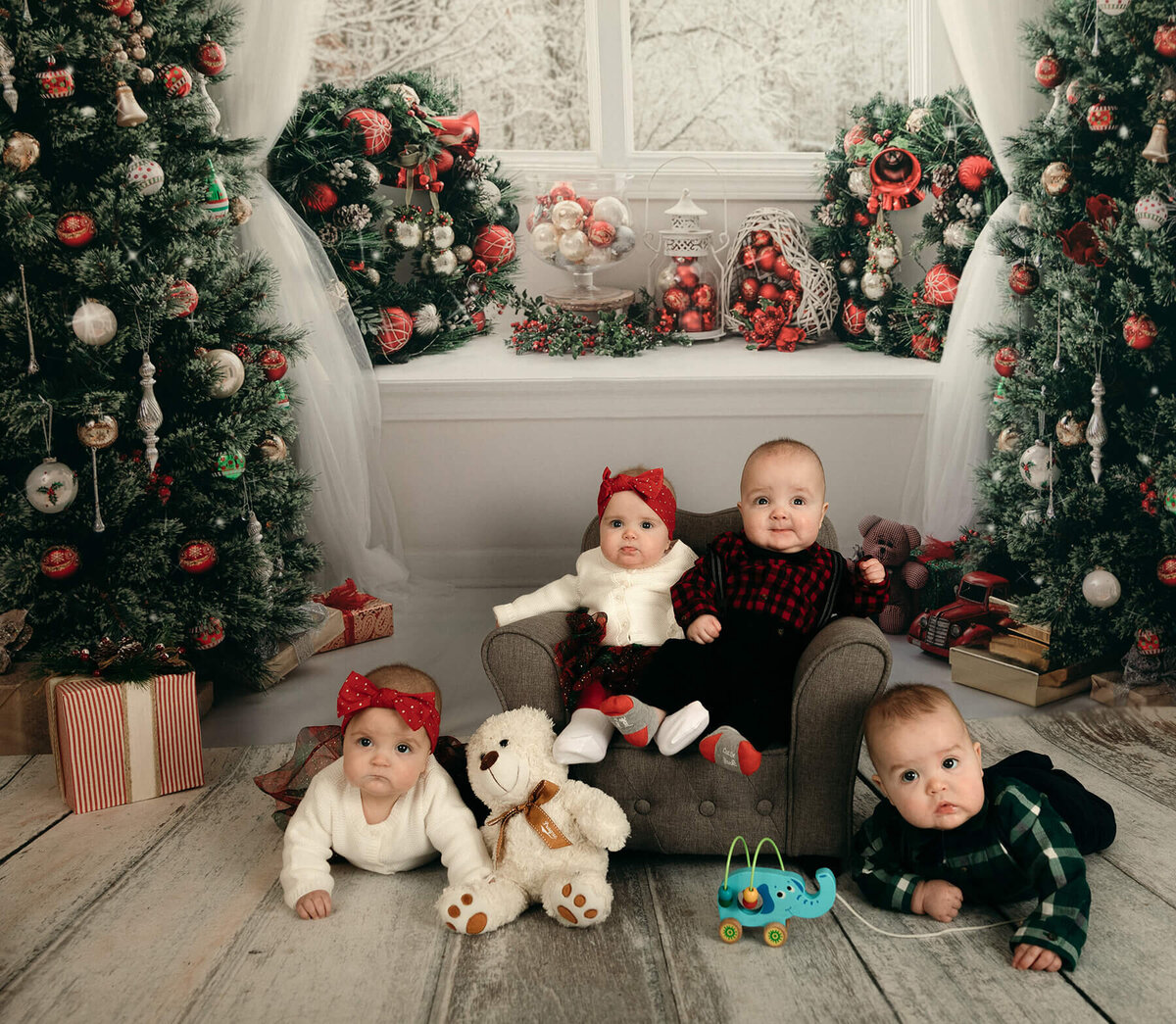 Quadruplets at 6 months old in Christmas outfits in front of Christmas background. 