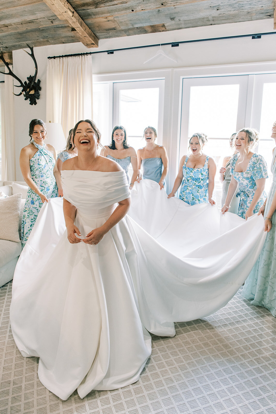  Bride and bridesmaids laughing while holding the gown train during getting-ready photos at a mountain rental home in Cashiers NC.