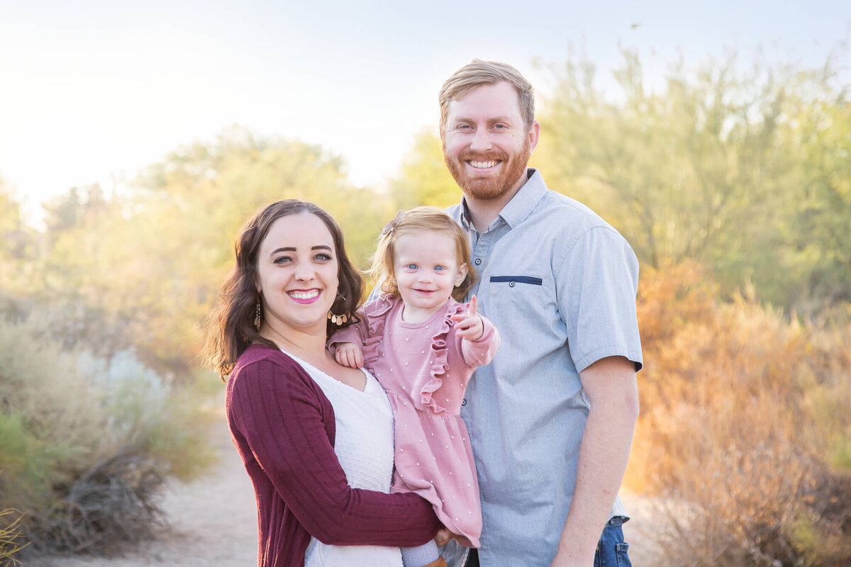 Redheaded man and brown haired woman holding redheaded toddler in desert park