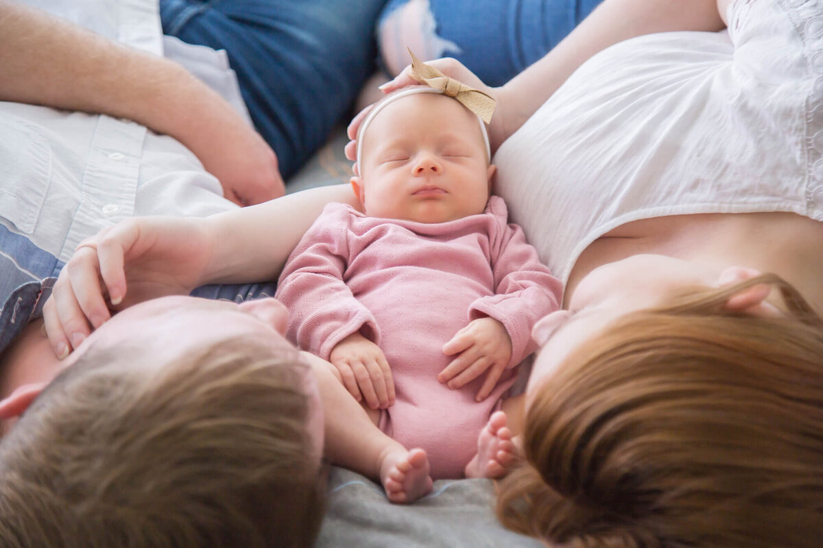 sleeping newborn baby girl on a bed between her parents